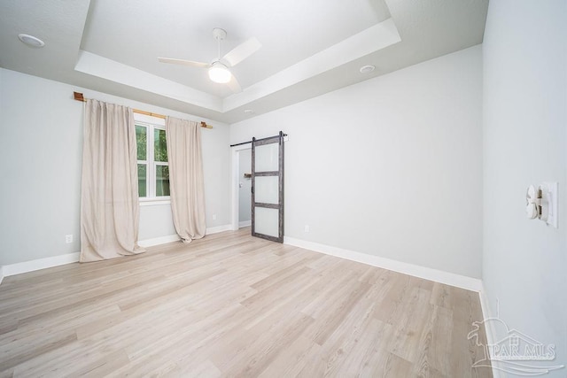 spare room with light hardwood / wood-style flooring, a barn door, a raised ceiling, and ceiling fan