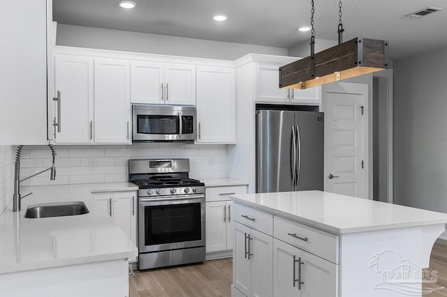 kitchen featuring light hardwood / wood-style floors, stainless steel appliances, a center island, tasteful backsplash, and white cabinetry