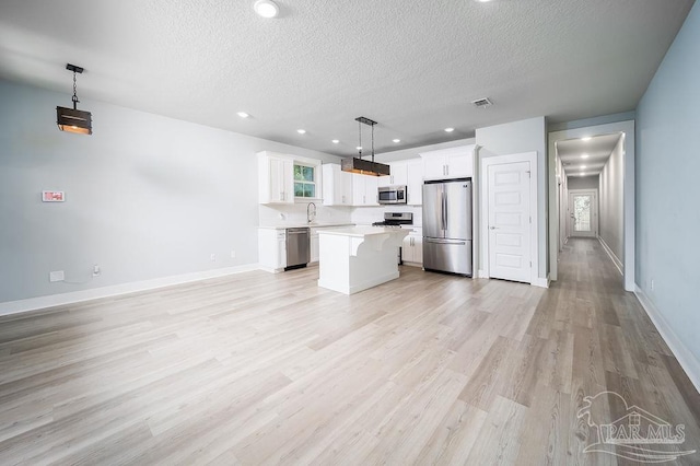 kitchen with light hardwood / wood-style floors, stainless steel appliances, white cabinets, a kitchen island, and pendant lighting