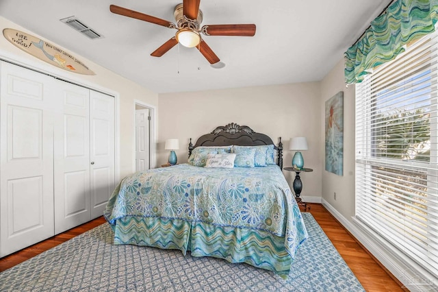 bedroom with a ceiling fan, wood finished floors, visible vents, baseboards, and a closet