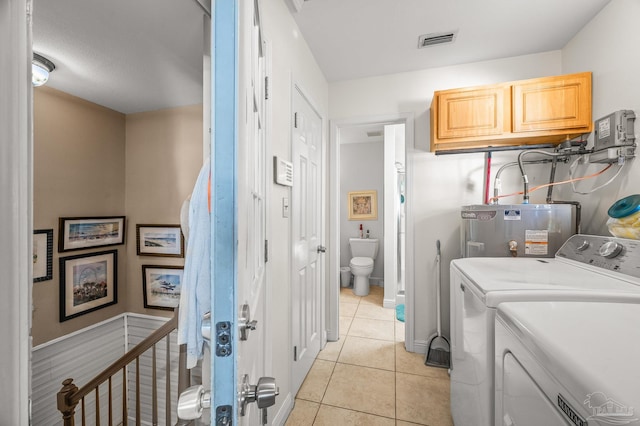 clothes washing area featuring visible vents, water heater, washer and dryer, light tile patterned flooring, and cabinet space