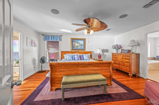 bedroom with connected bathroom, visible vents, baseboards, and wood finished floors