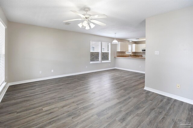 unfurnished living room with ceiling fan, dark wood-type flooring, and a textured ceiling