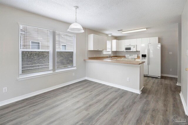 kitchen featuring hanging light fixtures, kitchen peninsula, wood-type flooring, white appliances, and white cabinets