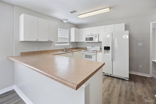 kitchen with kitchen peninsula, white appliances, a textured ceiling, wood-type flooring, and white cabinets