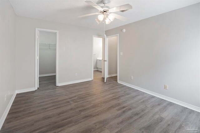 unfurnished bedroom with a walk in closet, a textured ceiling, ceiling fan, dark wood-type flooring, and a closet