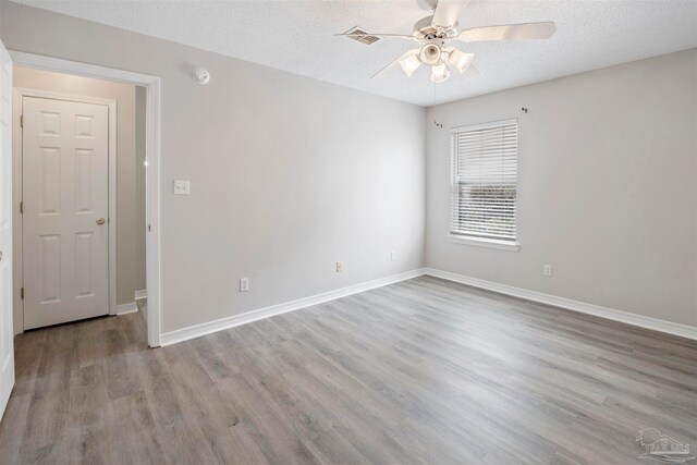 empty room with ceiling fan, light wood-type flooring, and a textured ceiling