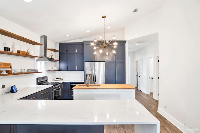 kitchen featuring tasteful backsplash, light stone counters, wall chimney exhaust hood, stainless steel appliances, and decorative light fixtures