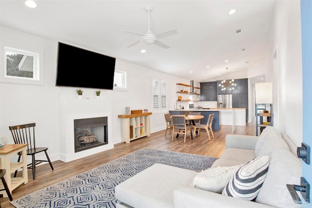 living room featuring wood-type flooring, ceiling fan with notable chandelier, and lofted ceiling