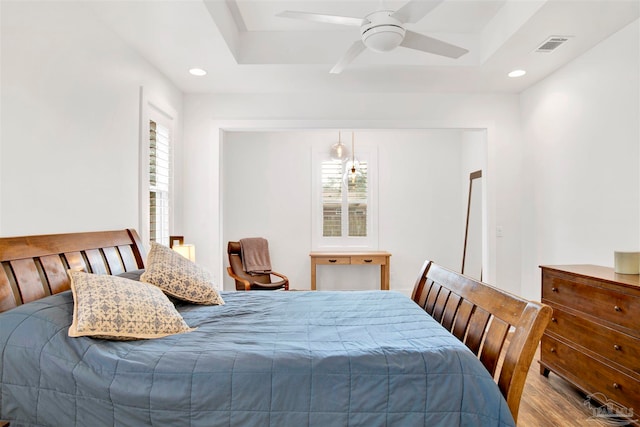 bedroom with a raised ceiling, ceiling fan, and light hardwood / wood-style floors