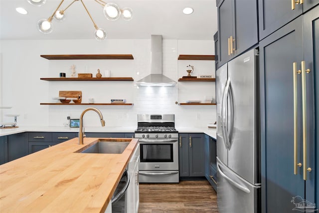 kitchen featuring butcher block counters, sink, wall chimney range hood, backsplash, and appliances with stainless steel finishes