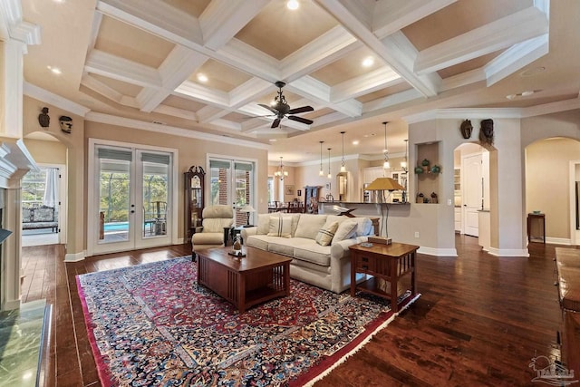 living room featuring ceiling fan with notable chandelier, coffered ceiling, beamed ceiling, dark wood-type flooring, and crown molding