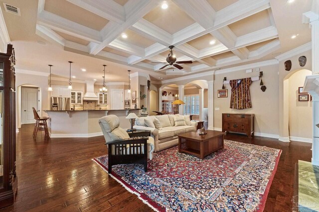 living room featuring ceiling fan, beamed ceiling, dark wood-type flooring, crown molding, and coffered ceiling