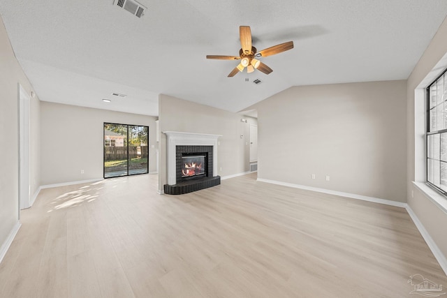 unfurnished living room featuring lofted ceiling, a brick fireplace, light hardwood / wood-style flooring, ceiling fan, and a textured ceiling