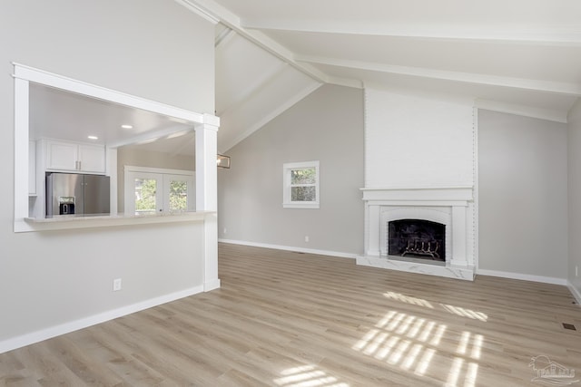 unfurnished living room with vaulted ceiling with beams, a fireplace, and light wood-type flooring