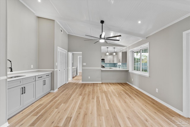 unfurnished living room with sink, ornamental molding, lofted ceiling with beams, light wood-type flooring, and ceiling fan