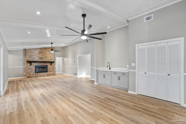 unfurnished living room featuring ceiling fan, light hardwood / wood-style floors, a fireplace, and vaulted ceiling with beams