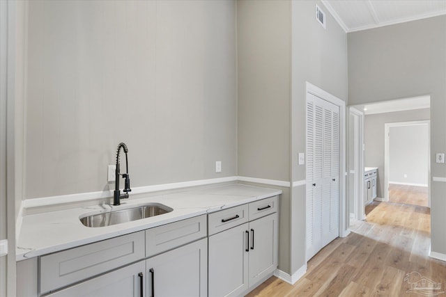 kitchen with light stone countertops, crown molding, light hardwood / wood-style floors, and sink