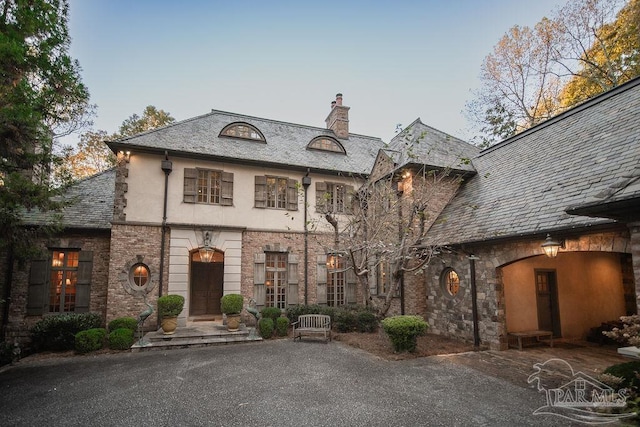 french provincial home with stucco siding, a high end roof, stone siding, and a chimney