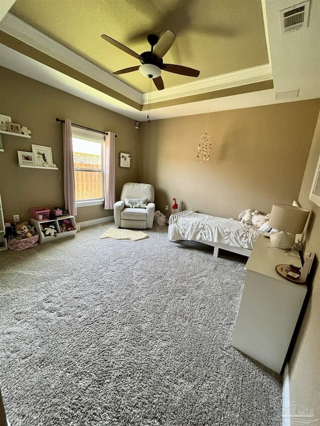 carpeted bedroom with a tray ceiling, visible vents, a ceiling fan, and ornamental molding
