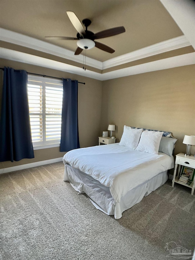 carpeted bedroom with ornamental molding, a raised ceiling, baseboards, and a ceiling fan