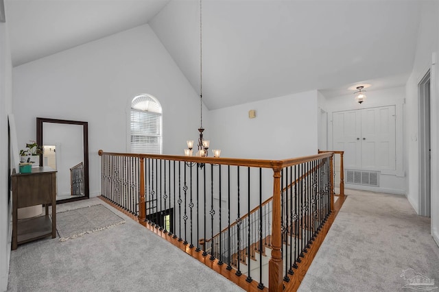 hallway with light colored carpet, a chandelier, and high vaulted ceiling