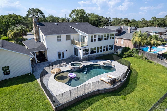 rear view of house with a patio, a balcony, a lawn, and a swimming pool with hot tub