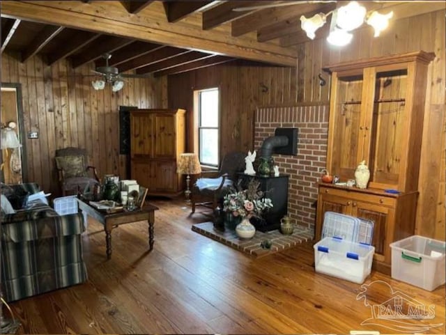 5301 Gentle Breeze Dr, Tallahassee, FL 32317 - living room featuring a wood stove, wood walls, beam ceiling, hardwood / wood-style flooring, and a ceiling fan
