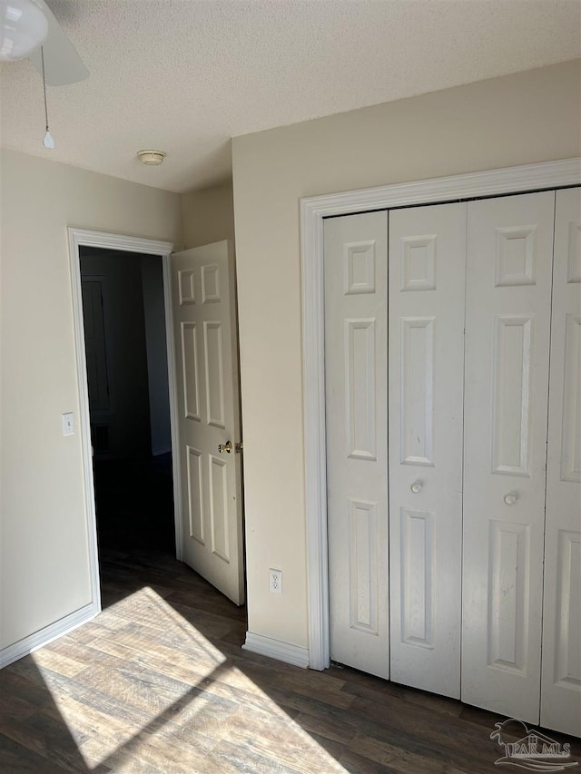 unfurnished bedroom featuring a textured ceiling, dark hardwood / wood-style flooring, a closet, and ceiling fan