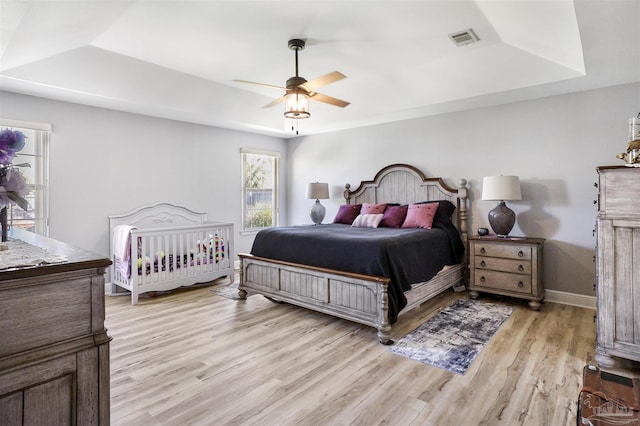 bedroom with visible vents, light wood-style flooring, baseboards, a raised ceiling, and ceiling fan