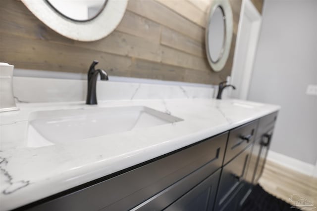 bathroom featuring double vanity, wood walls, wood finished floors, and a sink