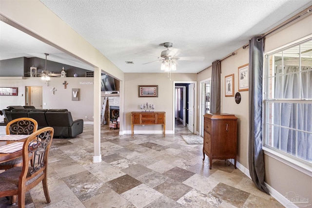 dining space featuring a healthy amount of sunlight, a fireplace, baseboards, and a ceiling fan