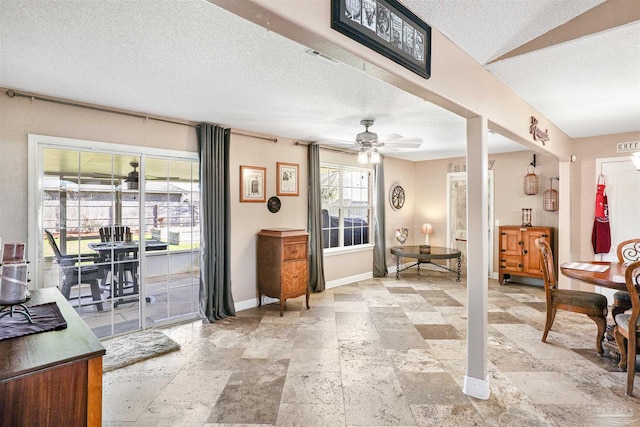 interior space with baseboards, a textured ceiling, stone tile floors, and a ceiling fan