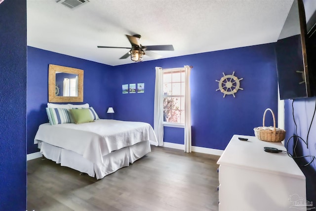 bedroom with visible vents, baseboards, wood finished floors, a textured ceiling, and a ceiling fan