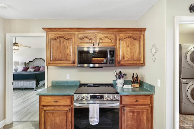 kitchen featuring dark countertops, brown cabinets, appliances with stainless steel finishes, and stacked washing maching and dryer