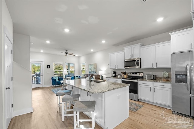 kitchen featuring light wood finished floors, appliances with stainless steel finishes, a sink, and white cabinetry