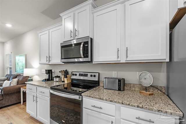 kitchen featuring stainless steel appliances, light wood-type flooring, open floor plan, and white cabinetry