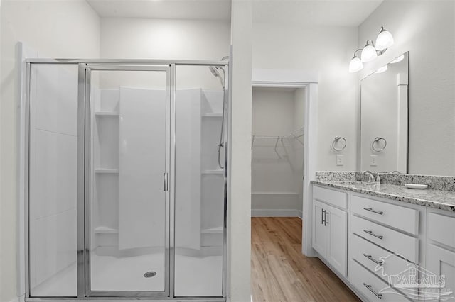 bathroom featuring a stall shower, wood finished floors, vanity, and a walk in closet