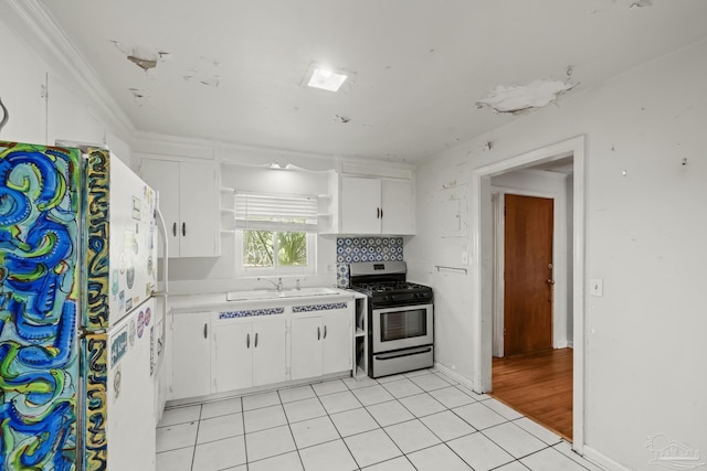 kitchen with light tile patterned floors, freestanding refrigerator, open shelves, a sink, and gas stove