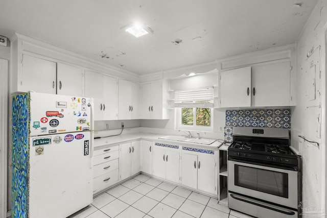 kitchen with light countertops, freestanding refrigerator, white cabinets, a sink, and gas range