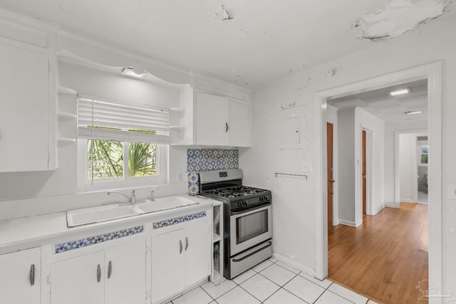 kitchen with stainless steel gas stove, open shelves, a sink, and white cabinets