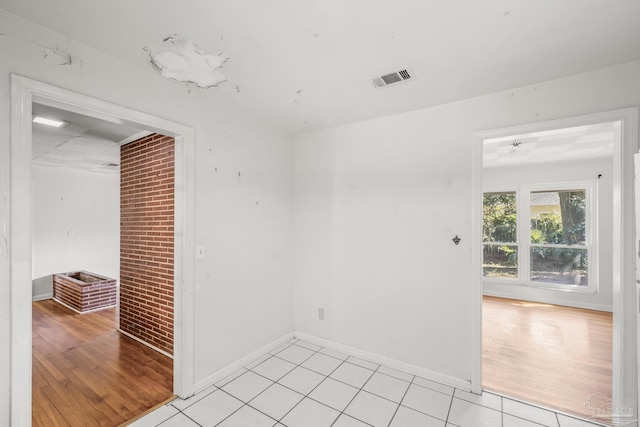 spare room featuring baseboards, visible vents, brick wall, and light tile patterned floors