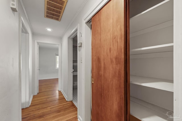 hallway featuring light wood-type flooring, visible vents, crown molding, and baseboards