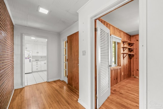 hallway with brick wall, ornamental molding, wood walls, and light wood-style flooring