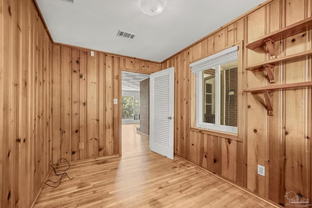 hallway with light wood-style floors, visible vents, and wood walls