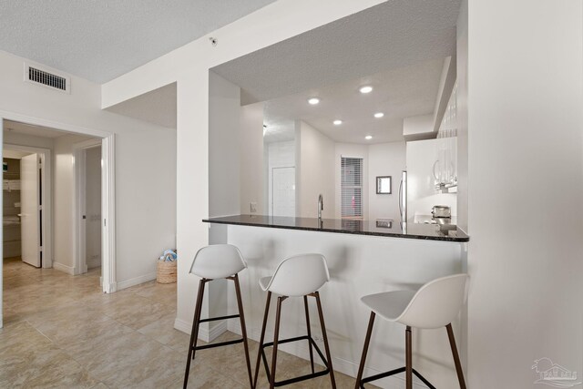 8501 Gulf Blvd Unit 3B, Navarre Beach, FL 32566 - kitchen with a kitchen breakfast bar, a peninsula, baseboards, dark countertops, and white cabinetry