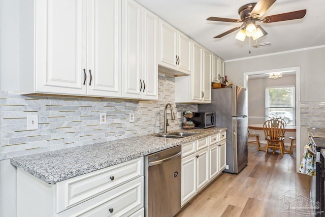 kitchen with white cabinets, a sink, stainless steel appliances, light wood-type flooring, and backsplash