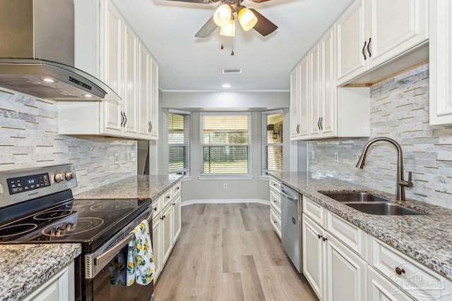 kitchen with stainless steel appliances, a sink, white cabinetry, light wood-type flooring, and wall chimney exhaust hood