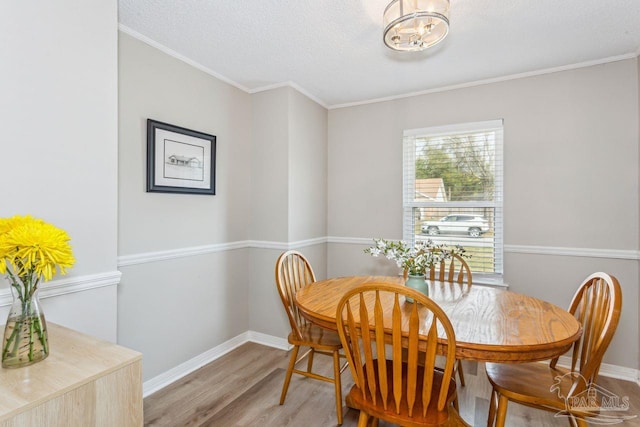 dining room with light wood-style floors, ornamental molding, a textured ceiling, and baseboards