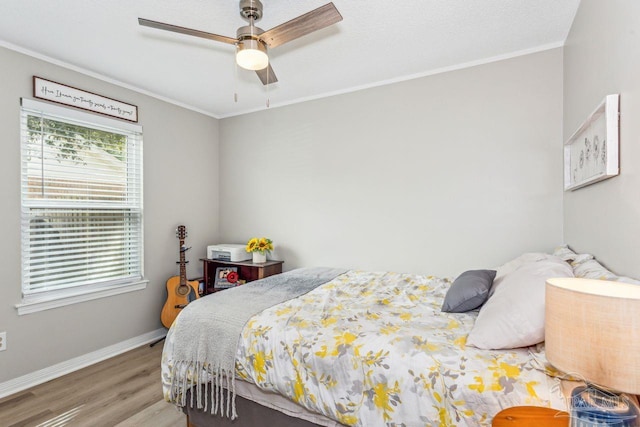 bedroom with a ceiling fan, crown molding, baseboards, and wood finished floors